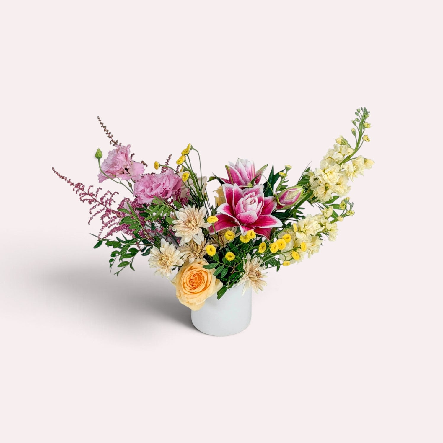A flower arrangement featuring shades of pink and yellow in a small white ceramic vase. Available for local delivery in Minneapolis.