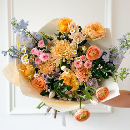 Hand-tied bouquet of colorful spring flowers including ranunculus, delphinium, feverfew, roses, cremons, spray roses, and tulips wrapped in premium korean flower wrapping paper. Send flowers as a gift idea