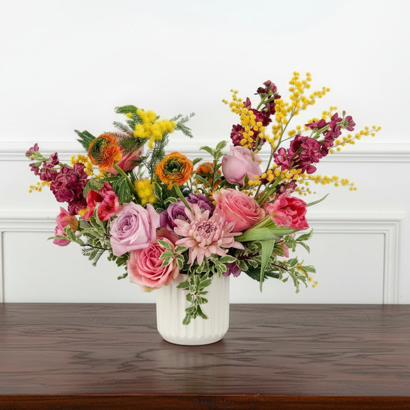 Colorful, bespoke floral arrangement featuring yellow Mimosa flower accents, pink garden roses, and orange ranunculus in a ceramic vase for Minnesota delivery or Edina pickup.