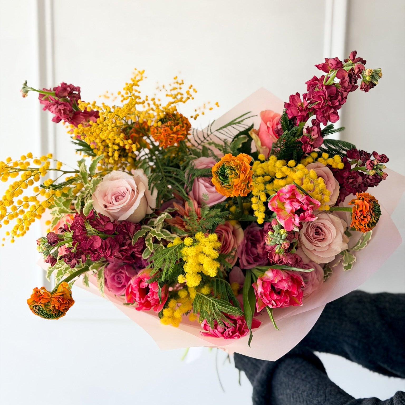 Breathtaking hand-tied garden bouquet featuring yellow Mimosa, pink ranunculus, and purple snapdragons, for March's Monthly Color Palette, wrapped in blush paper for International Women's Day.