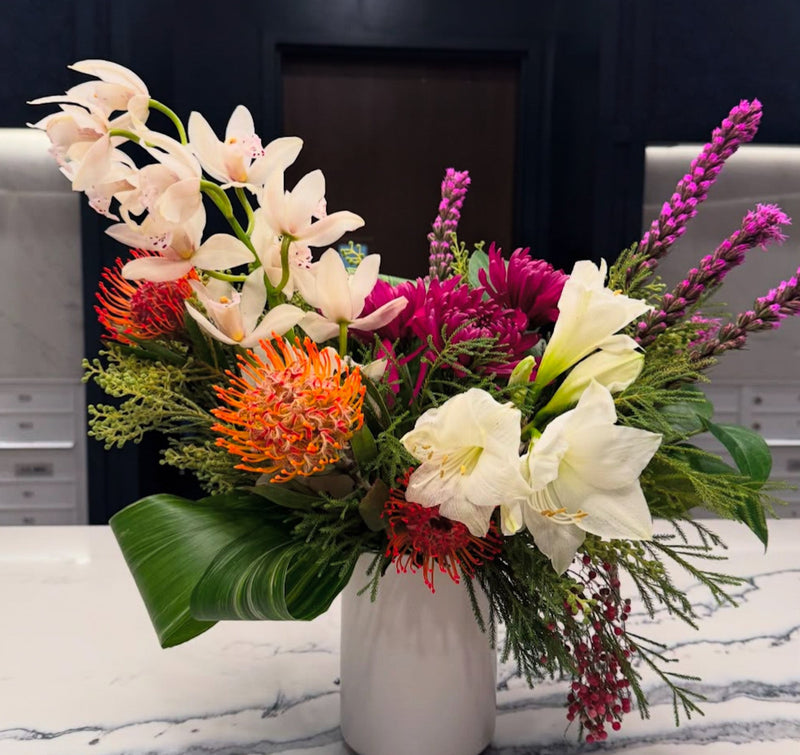 A colorful tropical arrangement of orchids, pin cushions, amaryllis, and liatris for a corporate lobby flower subscription. Luxury floral concierge service