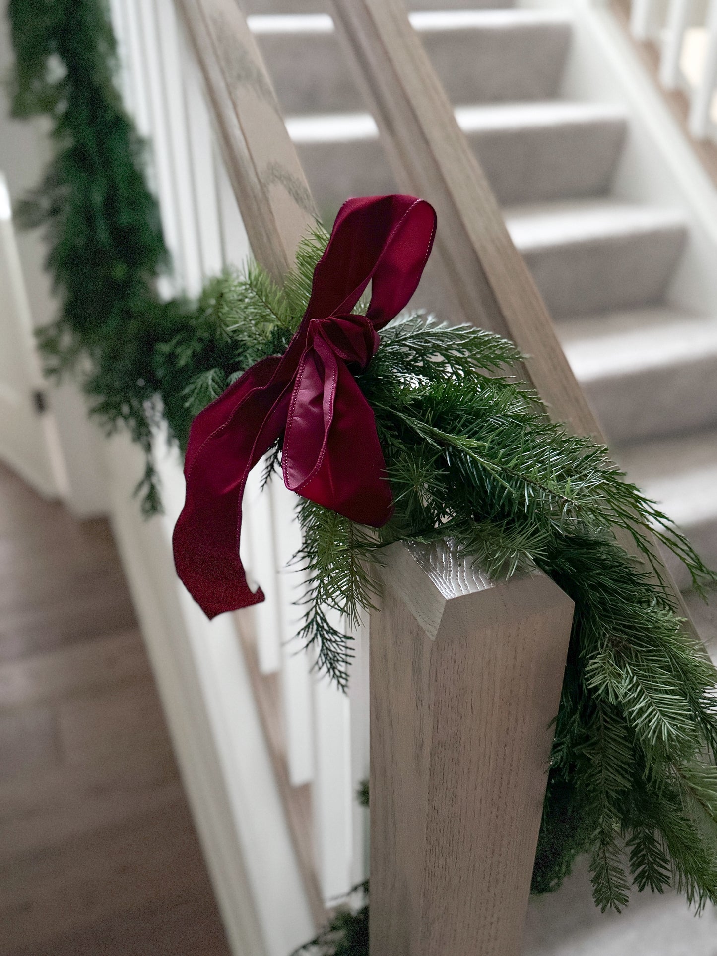 Detailed view of red bow on custom holiday garland featuring fresh greenery, perfect for mantels, staircases, or festive home décor, pick-up in Edina or local delivery