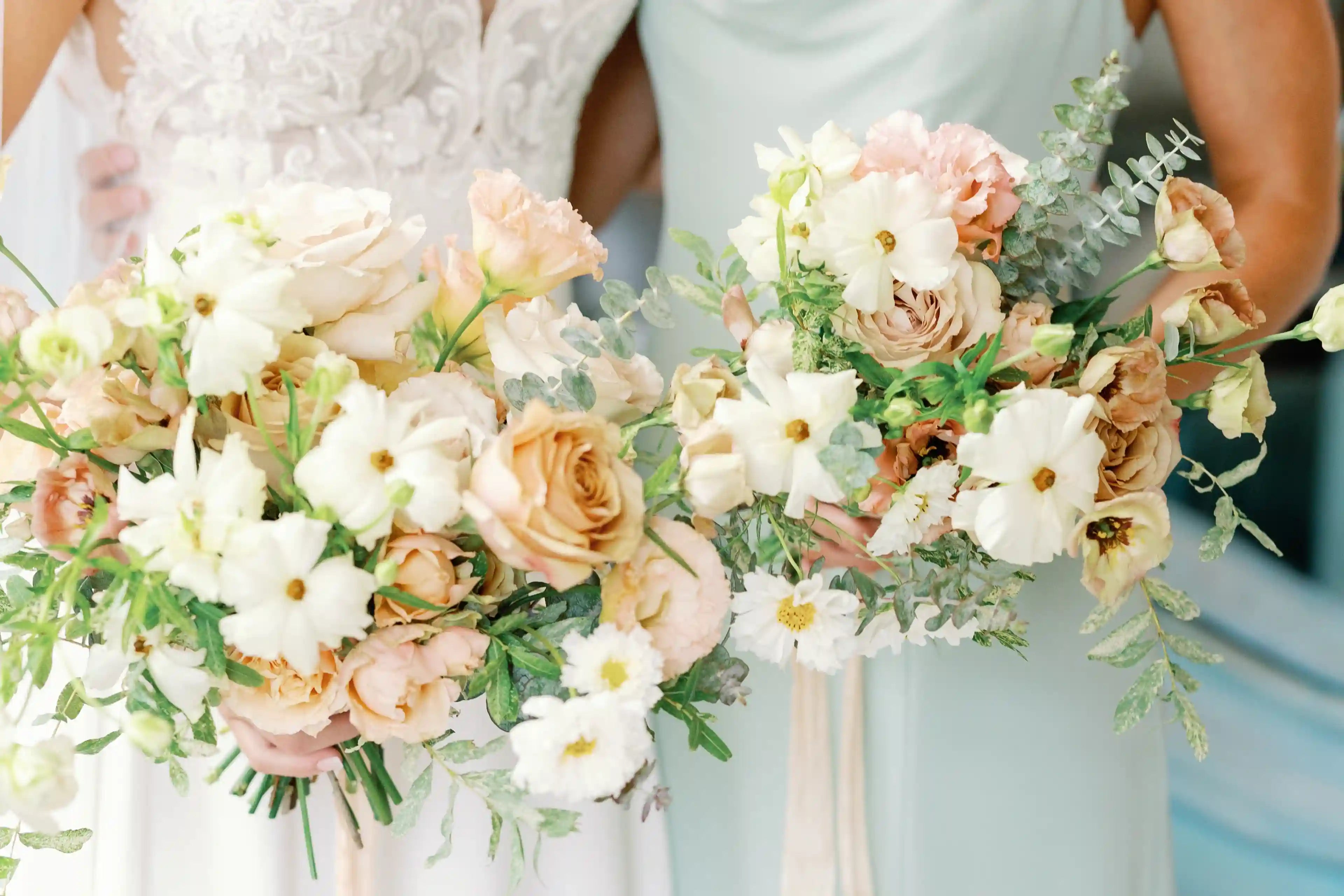 Bride and bridesmaid holding coordinating textured bouquets featuring white ranunculus, toffee-colored roses, and fresh eucalyptus foliage.
