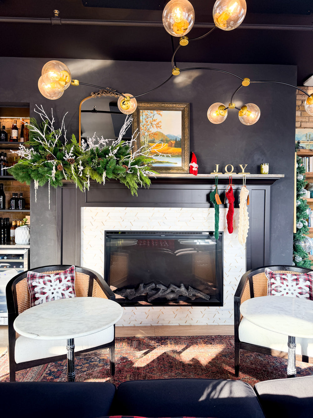 A cozy indoor living space centered around a dark fireplace with custom designed holiday greenery, stockings, and Christmas accents for a business. Custom commercial Christmas decorating service in Minneapolis.