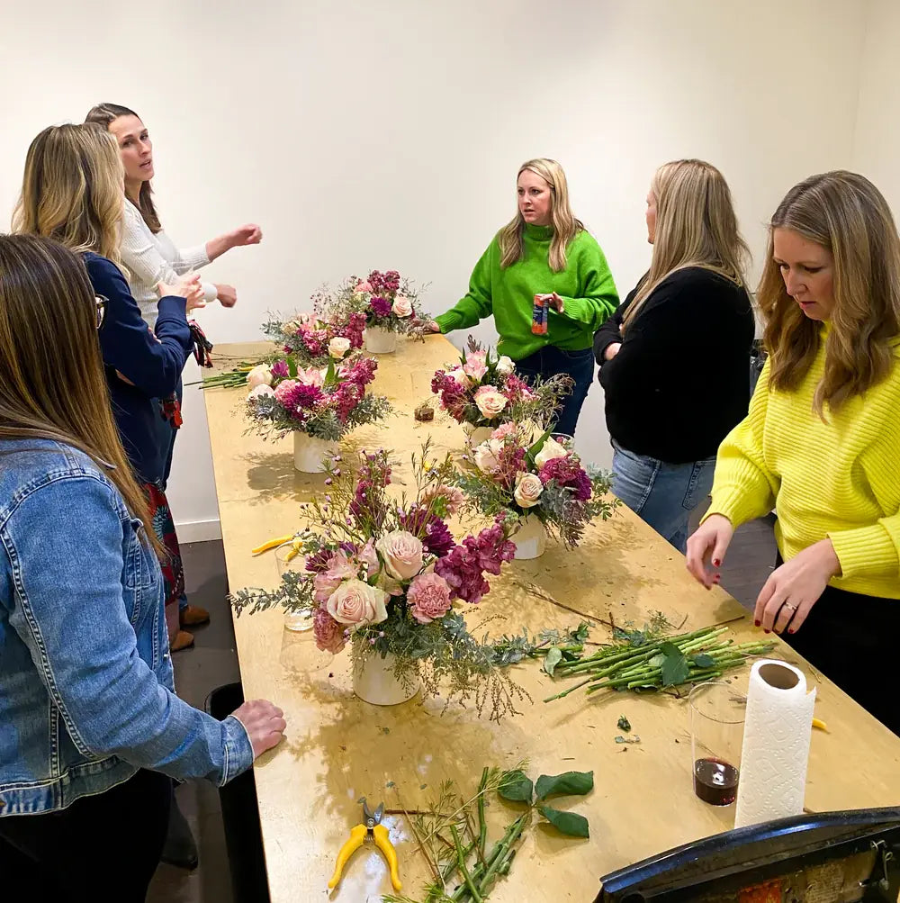 Participants learning flower arrangement techniques at a long wooden table during a floral design class at The Petal Floral Boutique.