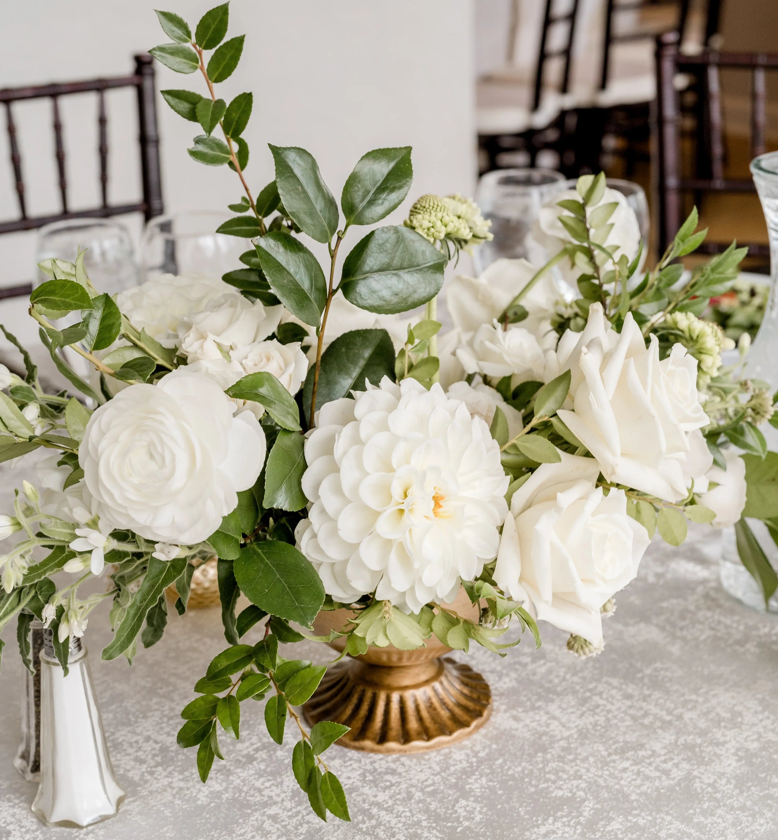 Floral wedding centerpiece with white flowers and greenery designed in a classic gold footed vase.