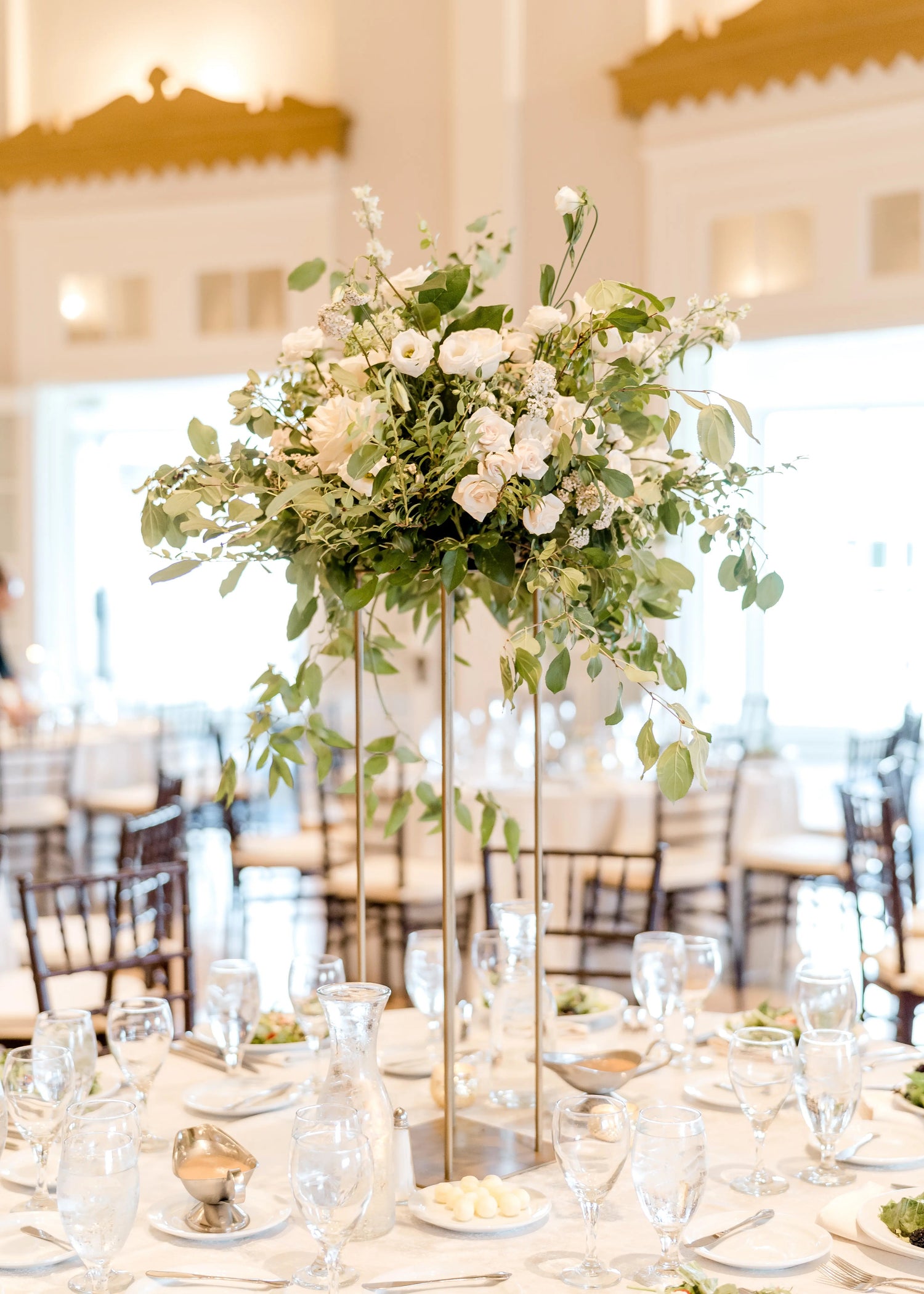 Elevated wedding floral centerpiece with sprawling greenery and beautiful white flowers in a upscale ballroom. 