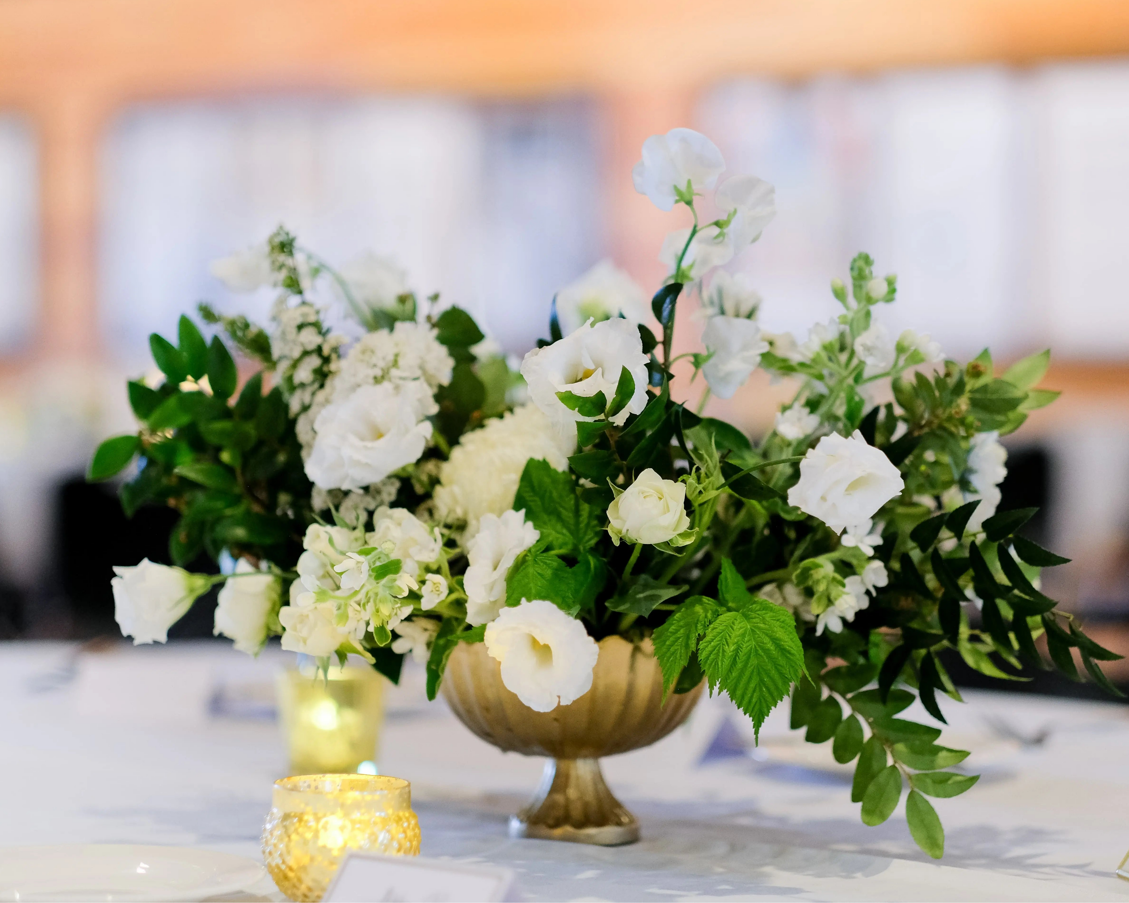 Breathtaking wedding centerpiece with white blooms and sprawling greenery in a deluxe compote vase.