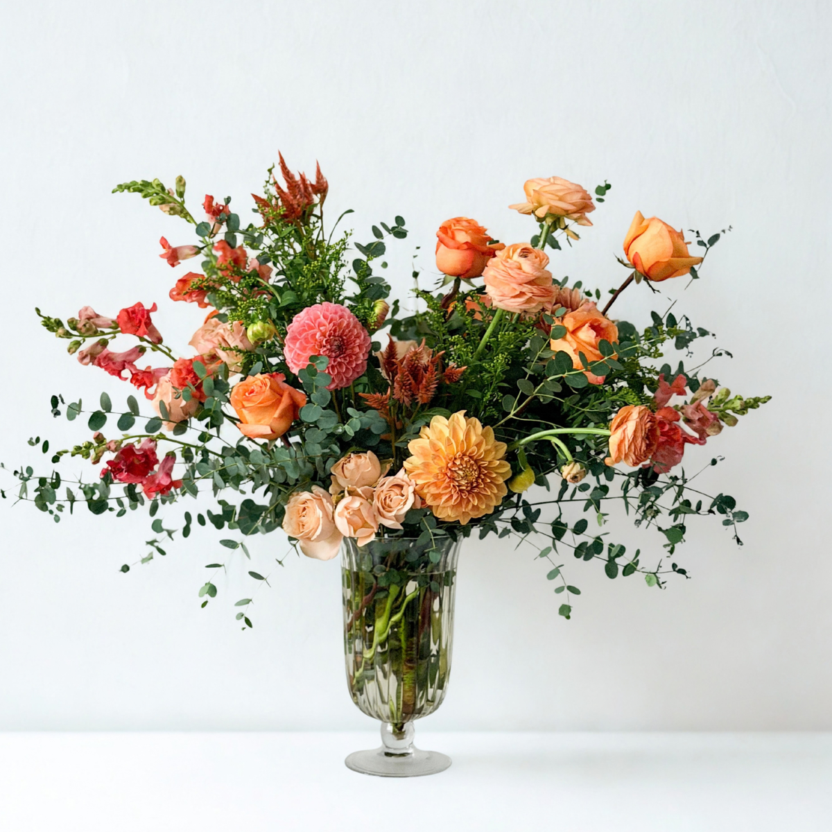 Premium October floral arrangement presented in a glass vase, showcasing a palette of bright coral, mauve, soft peach, and gentle orange accents balanced with fresh greenery. Available for local flower delivery in Minneapolis, Edina, Wayzata, and Minnetonka.