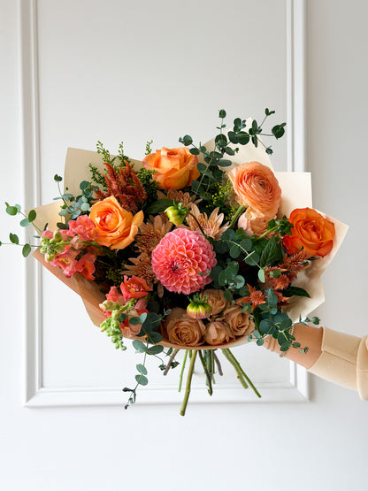 Signature October bouquet featuring a warm palette of bright coral, dusty mauve, soft peach, and gentle orange blooms balanced with fresh green foliage. Available for pickup in-store in Edina, or local delivery across Minneapolis, Bloomington, and Eden Prarie.