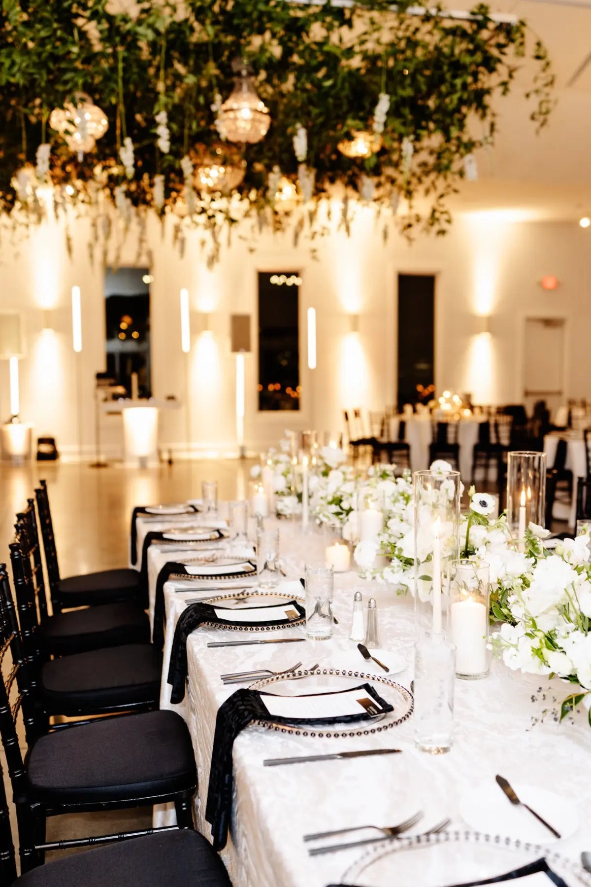 Elegant banquet hall with tables set for a beautiful, formal wedding, featuring a hanging floral installation by The Petal.