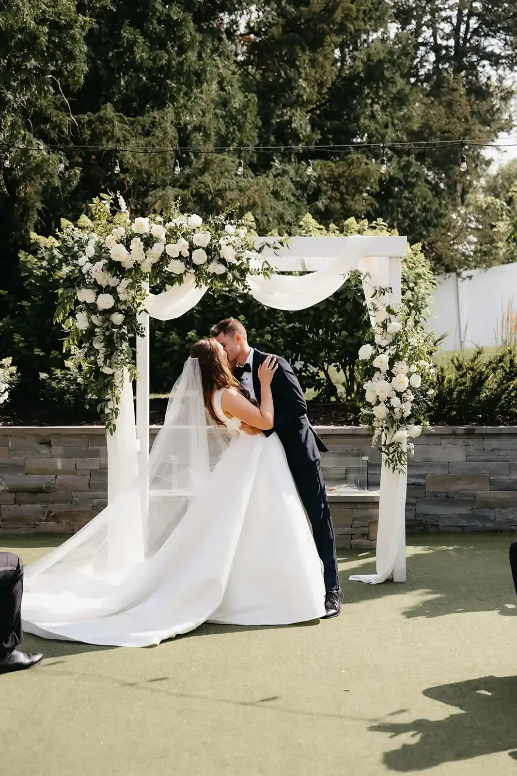 Wedding couple kissing under a floral archway with white and green floral sprays and romantic drapery for an outdoor wedding in Minneapolis