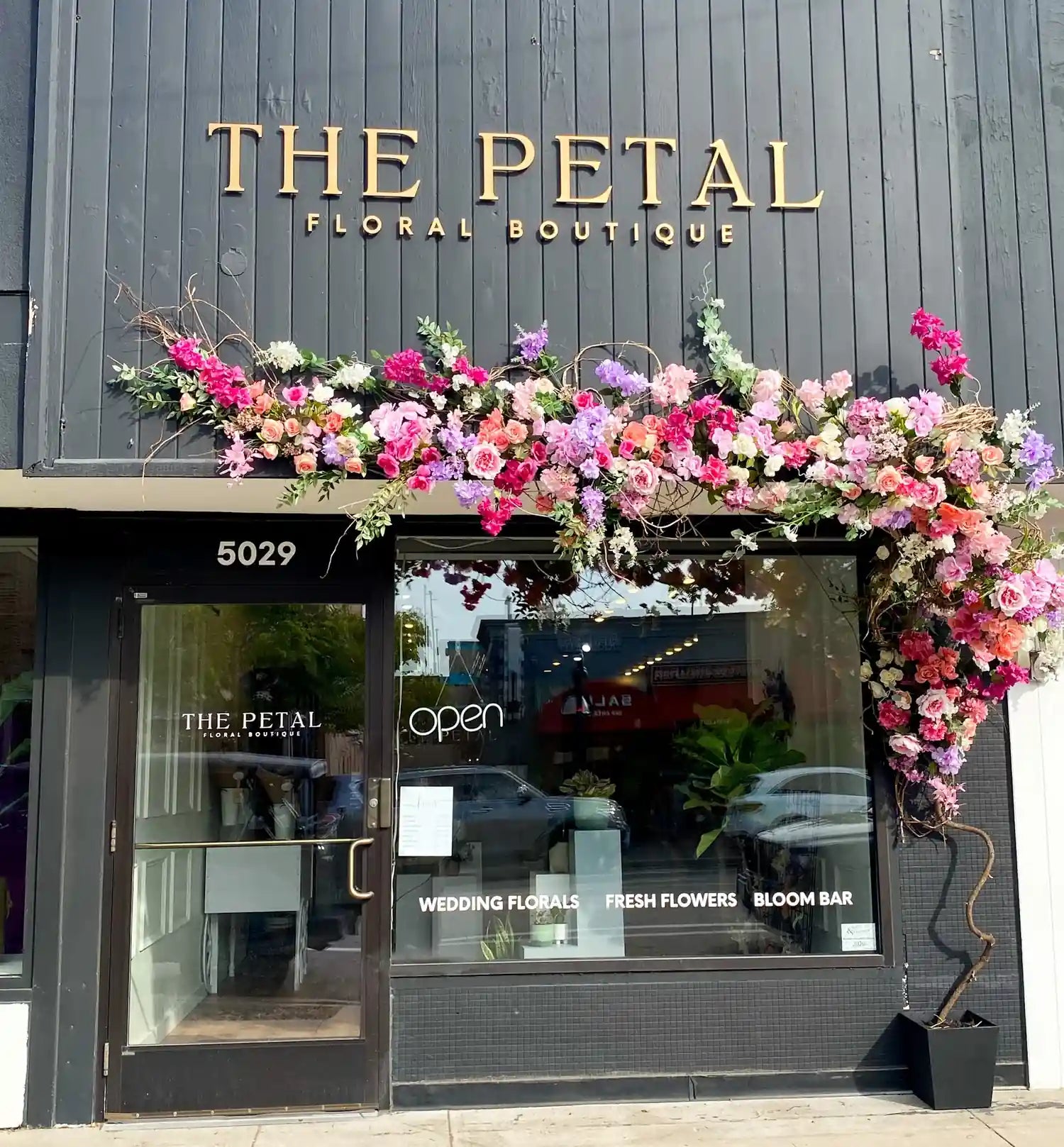 Exterior of The Petal Floral Boutique featuring a dark wood facade and a massive pink, purple, and white floral installation over the entrance.