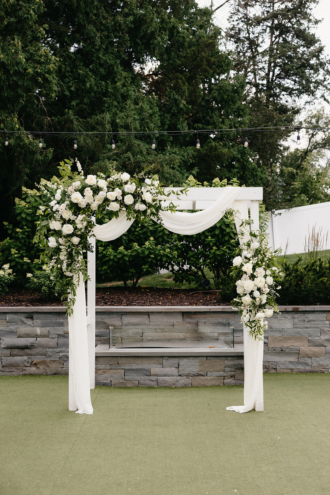 wedding ceremony arch with romantic drapery and white flowers with greenery for an outdoor wedding at hutton house in minneapolis