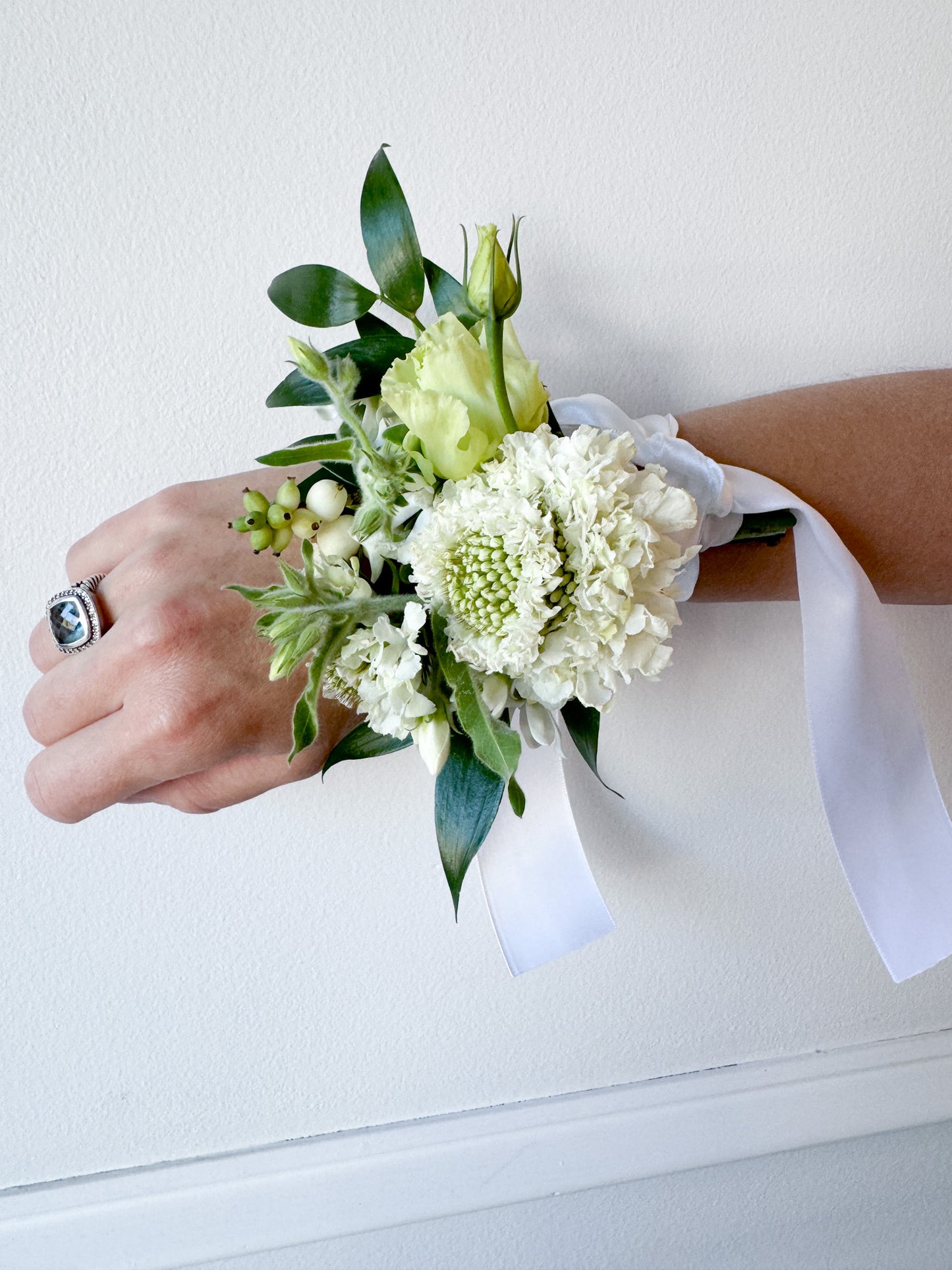 A white custom wrist corsage tied with a white ribbon.  Perfect for homecoming, prom or wedding.  