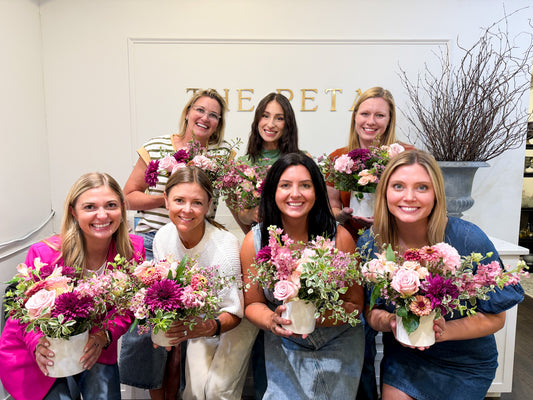 A group of floral workshop participants at THE PETAL Floral Boutique holding their floral centerpieces, smiling for the camera.